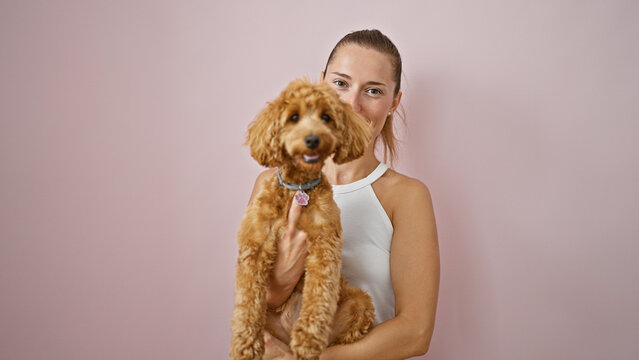Young caucasian woman with dog smiling hugging over isolated pink background