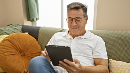 A middle-aged man relaxes at home, engaging with a tablet in his cozy living room.