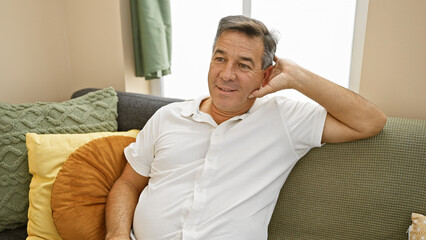 Obraz premium A relaxed middle-aged man sitting on a couch at home, with a content expression and comfortable modern decor.