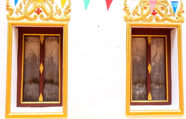 Ancient native style closed dark brown wood windows with peel off color on window and bright yellow frame on white wall cement of church, Thailand.