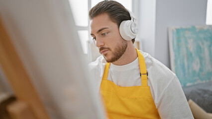 Young hispanic man artist listening to music drawing at art studio