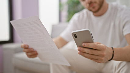 Young hispanic man reading document using smartphone at home