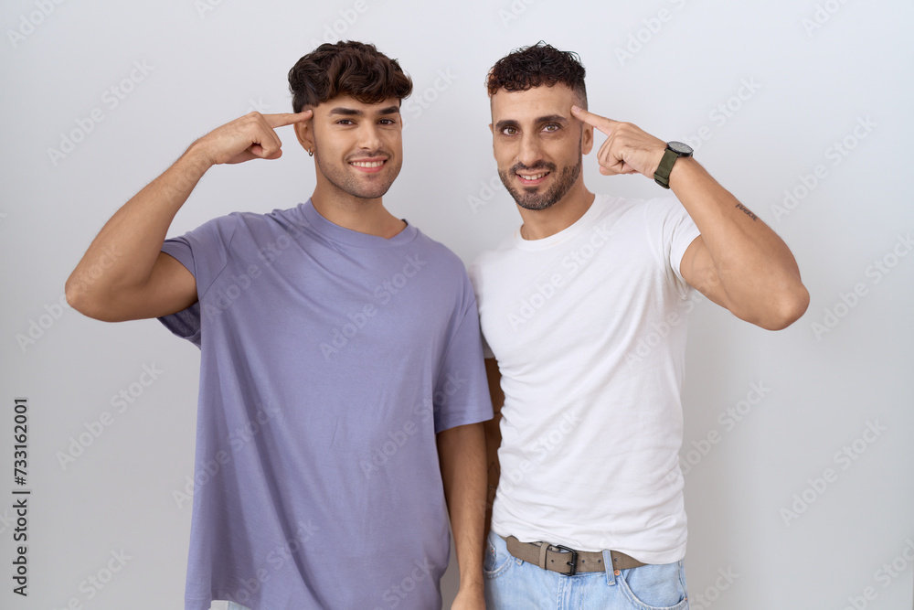 Poster Homosexual gay couple standing over white background smiling pointing to head with one finger, great idea or thought, good memory