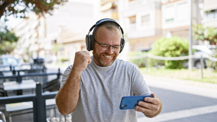Caucasian man watching video on smartphone celebrating at street