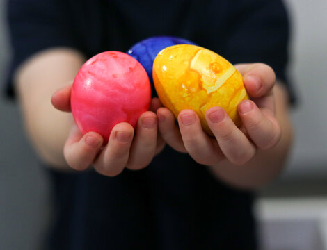 Close up of kids hands holding colored Easter eggs, blurry background
