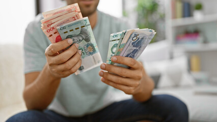 Indoor snapshot, dynamic young man making money count, sitting cozily on sofa at home, banking...