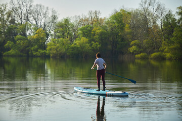 Fototapeta na wymiar A woman swims on a sapboard on the lake. Water entertainment.