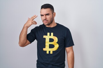 Young hispanic man wearing bitcoin t shirt shooting and killing oneself pointing hand and fingers...