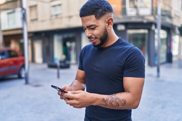 Young latin man smiling confident using smartphone at street