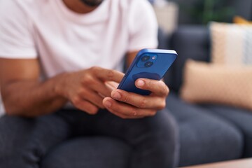 Young latin man using smartphone sitting on sofa at home