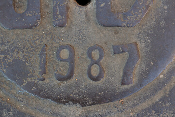 1987 years. Figures 1, 9, 8, 7 on gray rusty metal surface. Closeup street photo of fragment of old dirty sewer manhole with numbers marked in Georgian city of Tbilisi. Semicircular lines. Vintage