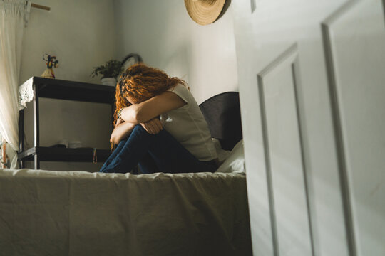 Fallen woman sitting on her bed covering herself at home. pain and sadness concept.