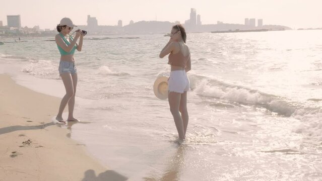 Two young female tourists taking pictures at the beach by the sea