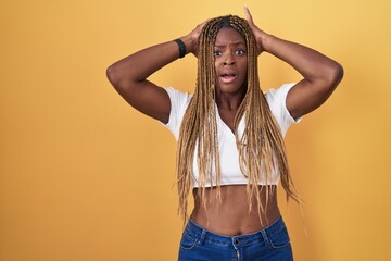 African american woman with braided hair standing over yellow background crazy and scared with...