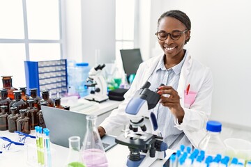 African american woman scientist using laptop and microscope at laboratory
