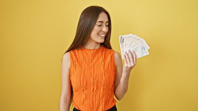 Smiling woman in orange top holding british pounds against a yellow background, portraying finance and happiness.