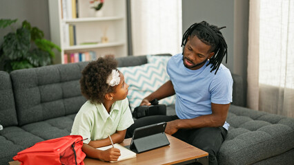 African american father and daughter sitting on sofa studying at home