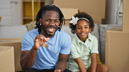 African american father and daughter holding new house keys sitting on sofa speaking at new home