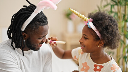 African american father and daughter wearing funny diadem applying makeup smiling at bedroom