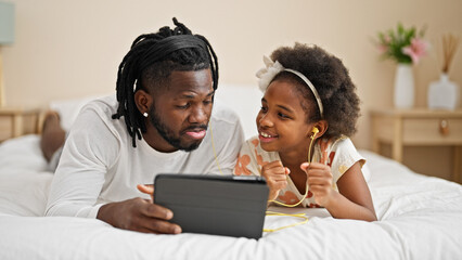 African american father and daughter listening to music lying on bed at bedroom
