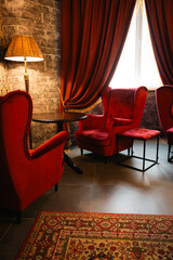 Red armchairs and table with lamp in cozy classic interior. Antique living room with red curtains...