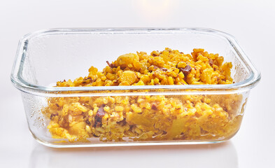 Golden saffron-infused rice with seafood and vegetables presented in a clear glass dish against a white background, depicting spanish cuisine.