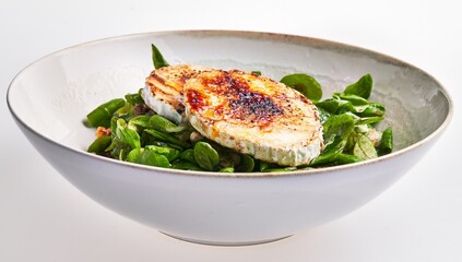 Grilled goat cheese on a bed of fresh spinach leaves served in a ceramic bowl on a white background.