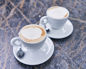 Two cappuccinos with frothy foam set against a marbled table background, reflecting a casual coffee break moment.