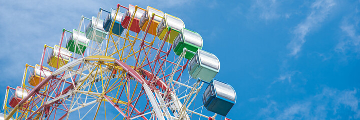 Panorama colorful sightseeing cabin or multiple passengers carrying components with support frame, rim of modern Ferris Wheel at amusement park in Nha Trang, Vietnam, blue sky, spoke cable