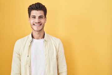 Young hispanic man standing over yellow background with a happy and cool smile on face. lucky...