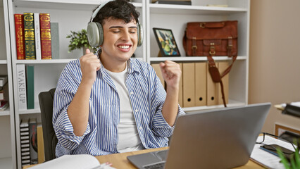 Happy man with headphones celebrating in a home office with laptop and books.