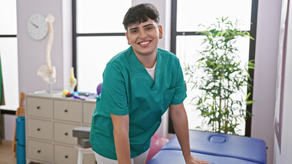 Fototapeta premium A smiling young man in green scrubs standing inside a bright rehab clinic room.
