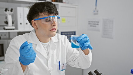 Focused man in lab coat analyzing blue chemical in beaker at indoor laboratory