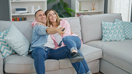 Man and woman couple sitting on sofa watching tv smiling at home