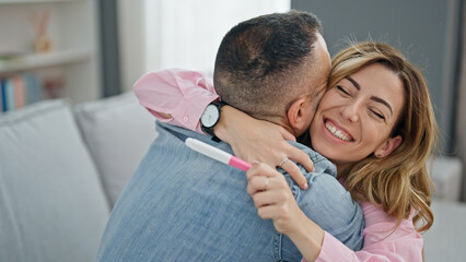 Man and woman couple holding pregnancy test celebrating at home - obrazy, fototapety, plakaty