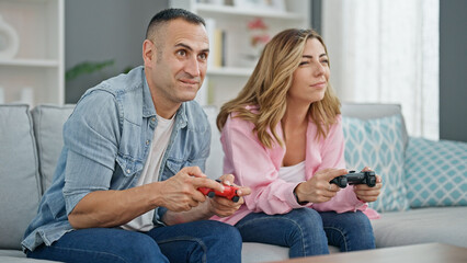 Man and woman couple playing video game sitting on sofa at home