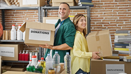 Man and woman volunteers holding donations packages smiling at charity center