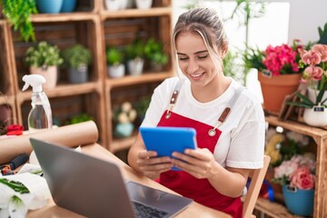 Young blonde woman florist smiling confident using laptop and touchpad at flower shop