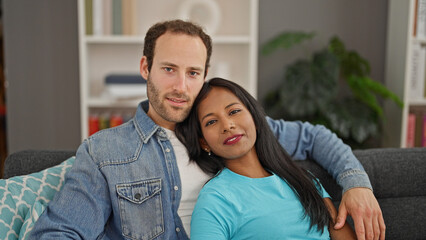 Fototapeta premium Beautiful couple hugging each other sitting on sofa with relaxed face at home