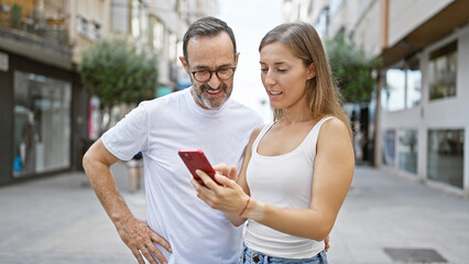 Cool and confident father smiling with daughter in their casual style, enjoying fun time together using smartphone on lively city street