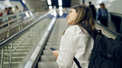 Young beautiful hispanic woman standing on escalator using smartphone in subway station of Madrid