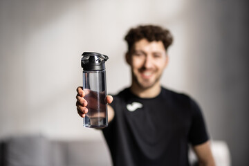 Sporty young man with headphones drinking water after his workout at home.