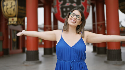 Joyful portrait of a beautiful hispanic woman in glasses, enjoying freedom with open arms at...