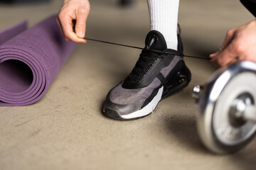Close up of man in fitness clothing fastening trainers before exercising with hand weights at home