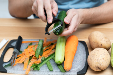 Close-up shot of a man peeling vegetables using special vegetable peelers in the kitchen