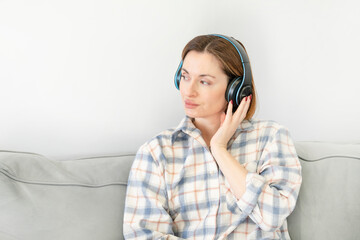 Beautiful woman in headphones holding smartphone and listening to music at home. Leisure time and relax concept