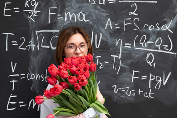 A young attractive teacher stands with a bouquet of flowers in the classroom. Teachers day and...