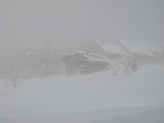 Fototapeta na wymiar chalets enneigés dans la brume en hiver situés vallée de Bellevaux dans les Alpes en Haute-Savoie