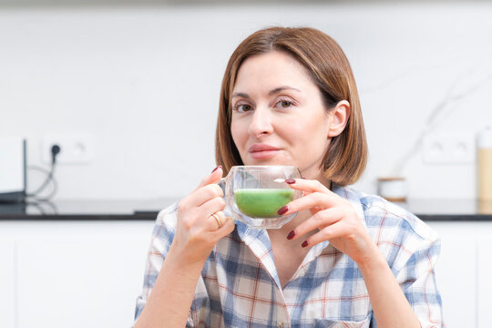 Close-up portrait of attractive girl drinking hot matcha tea in the kitchen