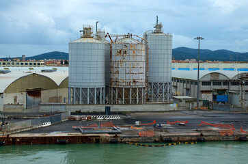Panoramic landscape view of commercial docks with silos and warehouses in port of Livorno. Import, export and business logistic. International water transport